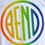 The emblem on White tee with a rainbow disc, a metal disc sculpture, and a red decal in the window, The Bend Store, May 27, 2023.