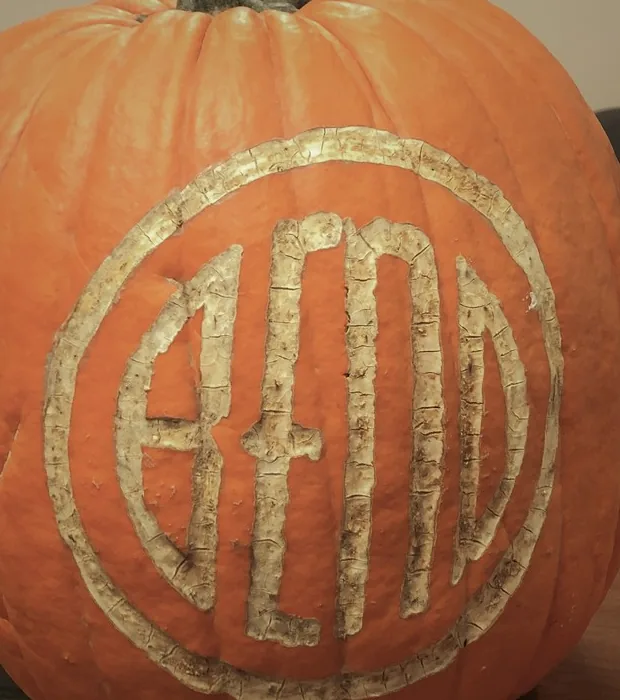 A pumpkin with a circular BEND emblem carved into its rind, the letters pale against the orange.