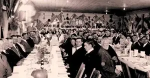 A long banquet table surrounded by guests, with flags hanging above them.