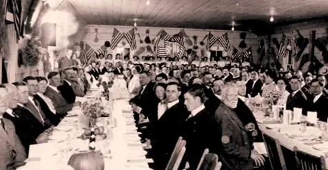 A long banquet table surrounded by guests, with flags hanging above them.