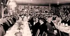 A long banquet table surrounded by guests, with flags hanging above them.