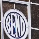 A circular panel on a dark tiled wall, the word BEND filling it in light narrow capitals inside a light ring.