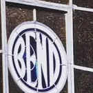 A circular panel on a dark tiled wall, the word BEND filling it in light narrow capitals inside a light ring.