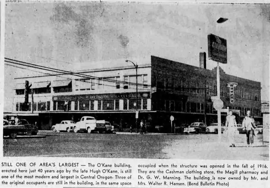 A street photograph of the two-story O’Kane Building with parked cars and its original storefront arrangement.