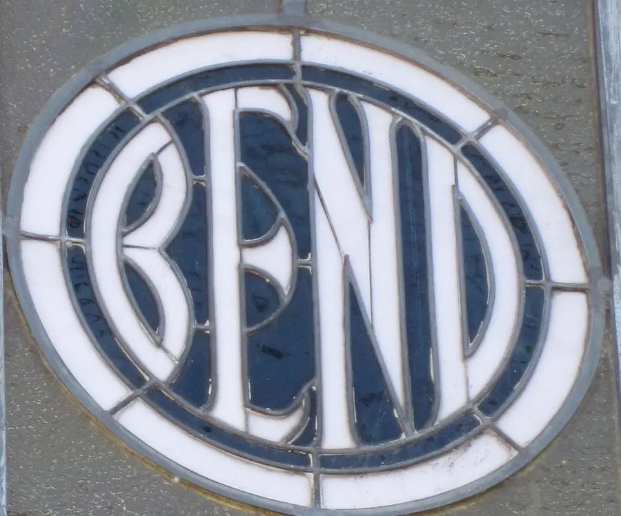 White BEND letters reading across a dark oval of stained glass, set in a leaded square in a pebbled transom.