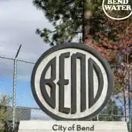 A circular sign carrying the BEND emblem in relief, above a stone base reading City of Bend.
