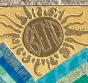 A yellow artwork on a brick wall, showing a Bend-emblem sun above mountains, water and trees.