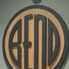 A large wooden disc on a wall, the word BEND cut into its tan face inside a dark ring.