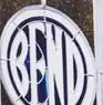 A circular panel on a dark tiled wall, the word BEND filling it in light narrow capitals inside a light ring.