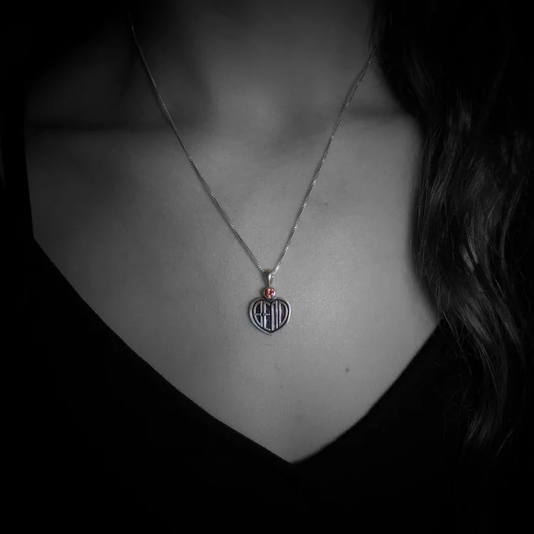 A silver necklace with a small heart-shaped Bend pendant and reddish stone.